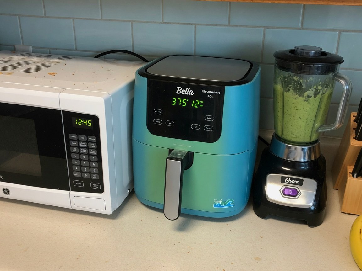 Bella Fits-anywhere slim 4qt air fryer in a blue-green Surf colorway nestled in a narrow gap between a microwave and a